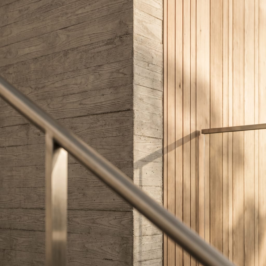 Détail de façade contemporaine en béton banché et bardage vertical en sapin de Douglas, ombres matinales